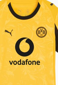 Maglia sportiva gialla con motivo floreale, dettagli neri, logo Puma, logo circolare Vodafone e emblema BVB 09. Maniche corte, collo rotondo.
