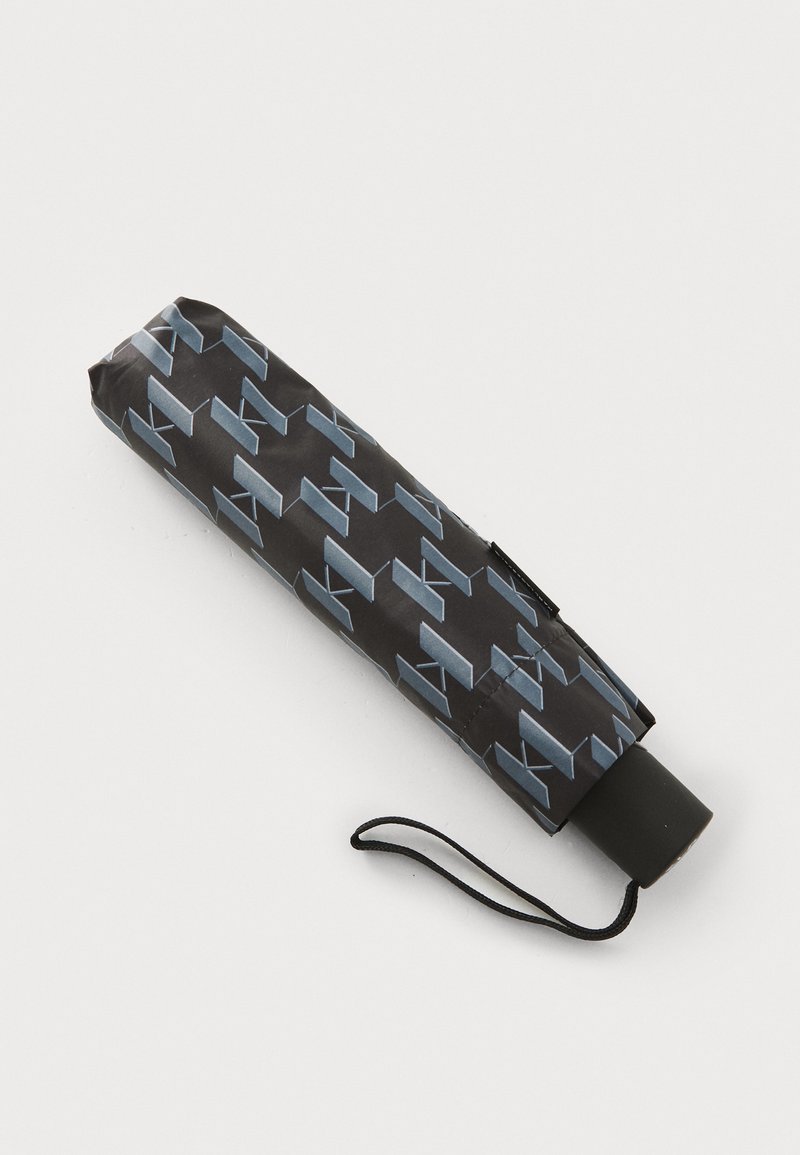 Kompakt svart paraply med blå geometrisk mønster, slank sylinderform, utstyrt med svart håndtak og håndleddsstropp for enkel bæring.