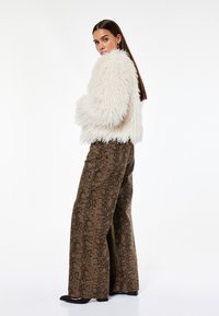 Biała puszysta kurtka zestawiona z brązowymi, wzorzystymi spodniami w stylu wide-leg z motywem skóry węża; czarne, szpiczaste buty dopełniają całość.