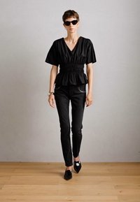 Crna peplum majica s kratkim rukavima, s naboranom strukom; uparena s uskim crnim trapericama i cipelama s oštrim vrhom. Sveukupno elegantan dizajn.