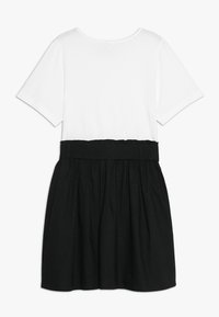 Lyhythihainen mekko, jossa on valkoinen yläosa ja musta hame, rypistetty vyötärö ja kontrastivärit. Pehmeä pinta koko mekossa.