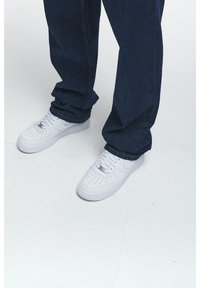 Zapatillas de cuero blancas con perforaciones en la caja de los dedos, combinadas con pantalones de mezclilla azul oscuro y dobladillo vuelto.