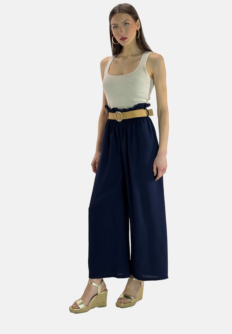 Marine wijd-naar-boven broek met een gerimpelde elastische tailleband, gecombineerd met een lichtbeige tanktop en gouden sleehakken.
