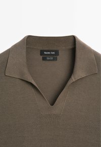 Polo shirt in cotone di un verde oliva tenue, con scollo a V e colletto classico. L'etichetta riporta "Massimo Dutti", indicando il marchio e la composizione.