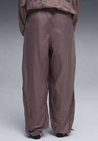 Pantalons amples et légers dans une teinte mauve discrète. Confectionnés en tissu lisse avec un léger éclat, comprenant des poches zippées et des poignets ajustables.