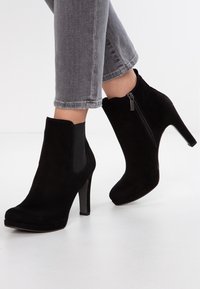 Czarne zamszowe botki za kostkę na wysokim obcasie, z elastycznymi panelami po bokach i zamkiem błyskawicznym z jednej strony. Gładka faktura z zaokrąglonym noskiem.