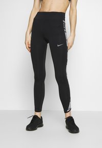 Leggings negras de cintura alta hechas de tela elástica, con un panel lateral gris que presenta la marca Nike impresa y un acabado liso y elegante.