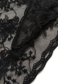 Sort blonde stof med blomstermønster, gennemsigtighed, bølgede kanter og intrikate detaljer. Baggrunden er en lys grå tekstur.