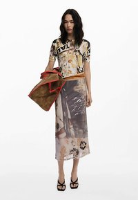 Trykt top med blomster- og grafiske mønstre, kombineret med et gennemsigtigt, mønstret langt skørt. Brun taske med røde accenter, højhælede sandaler.