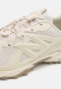 Hellbeige Sportschuh mit Mesh-Obermaterial, strukturierten synthetischen Akzenten, sicherem Schnürsystem und robustem Gummilaufsohle für Traktion.