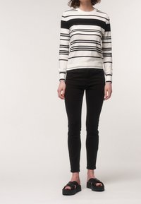 Černobílý pruhovaný svetr s dlouhým rukávem a kulatým výstřihem, kombinovaný s černými úzkými džíny a mohutnými černými sandály na platformě.