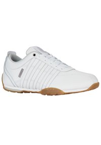 Bílé sportovní boty vyrobené z hladkého syntetického materiálu s šněrovacím designem, které mají tři charakteristické pruhy a gumovou podešev.