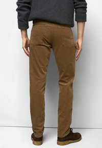 Pantalons en velours côtelé marron avec une coupe droite, comprenant deux poches arrière et une finition texturée, associés à des chaussures foncées.
