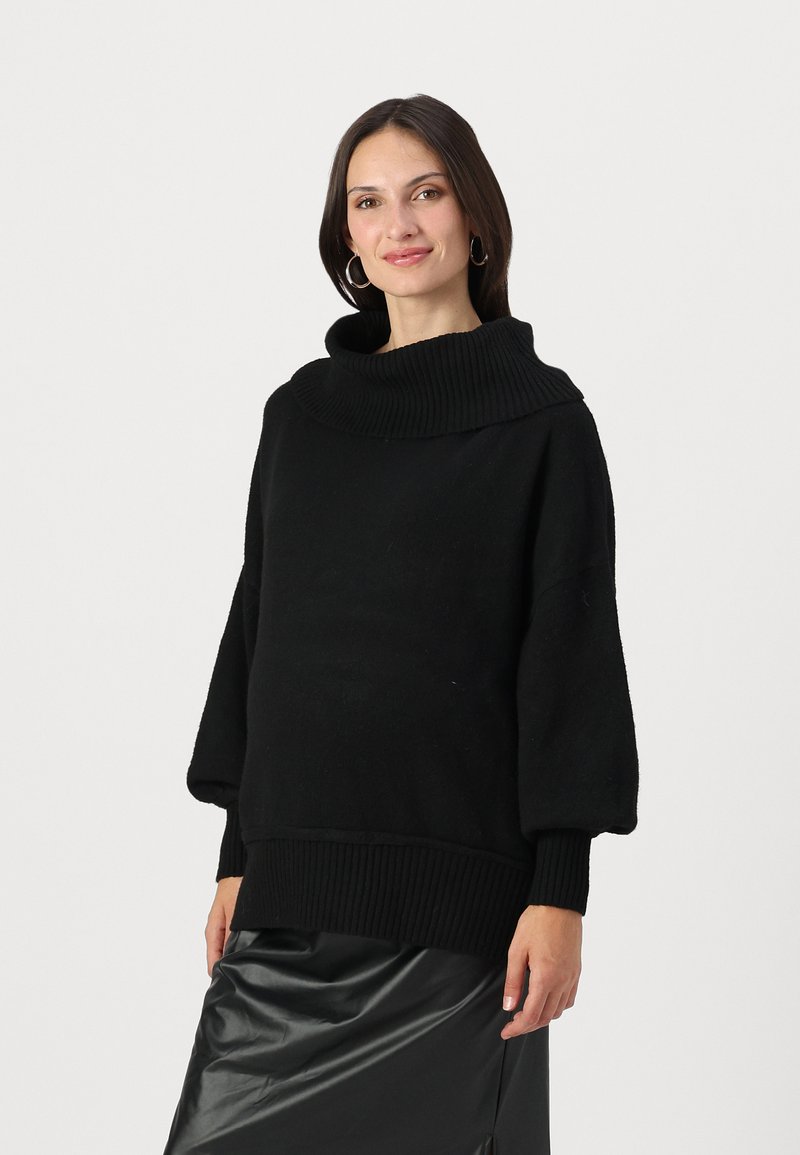 Pull noir surdimensionné avec un col à côtes, des manches bouffantes et un tricot texturé. Porté avec une jupe en cuir noir.