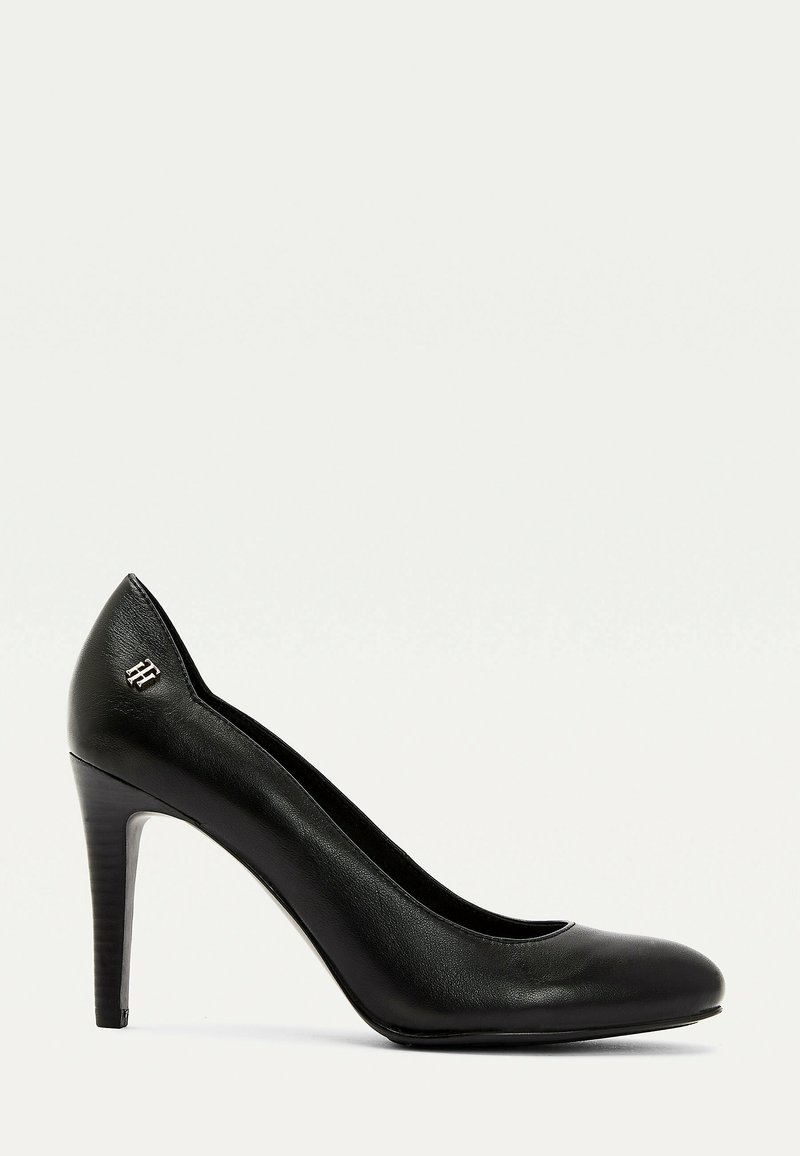 Escarpin en cuir noir à talon haut avec bout arrondi et petit logo métallique près du talon, présenté de profil sur un fond blanc.