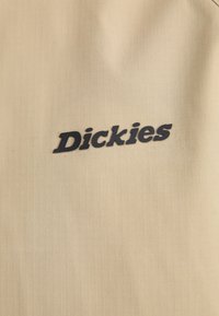 Bežna tkanina s suptilnom mrežastom teksturom sadrži istaknuti crni logo "Dickies".