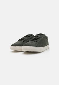 Zapatillas de ante verde con un diseño de caña baja, que presentan suelas de goma blanca y cordones planos, mostrando un material texturizado y costuras simples.