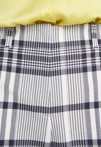 Chemise jaune rentrée dans un pantalon à carreaux noir et blanc avec des passants de ceinture visibles à la taille.