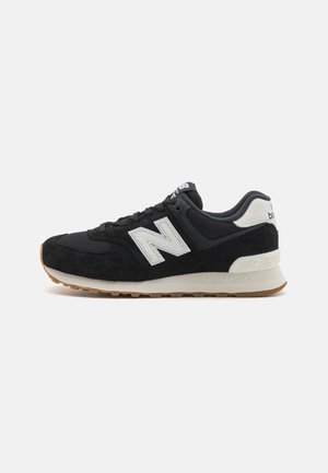 Baskets New Balance noir et blanc avec dessus en mesh et daim, logo blanc et semelle en caoutchouc naturel, montrées de profil sur fond blanc.