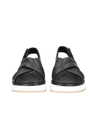 Sandales en cuir noir avec des lanières croisées, bout ouvert et semelle blanche avec des accents marron clair. Texture lisse et détails minimalistes.