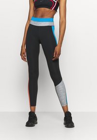 Czarne legginsy z różnymi kolorami: szarością, niebieskimi i pomarańczowymi akcentami. Elastyczny materiał, dopasowany kształt i zwężający się fason.