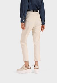 Jeans recortados de un color beige claro con dobladillo deshilachado, complementados con una camisa de mezclilla oscura de manga larga y zapatillas blancas gruesas con detalles dorados.