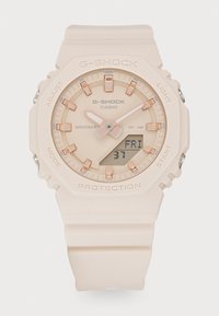 Casio G-Shock klokke med lys rosa resinrem, rund urskive, rosegulldetaljer, analoge og digitale skjermer, samt vanntetthetsmerke.