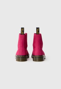 Bottes cheville en cuir fuchsia avec une texture lisse, couture jaune et étiquettes noires en boucle portant le texte "AVEC ÉLAN" à l'arrière.