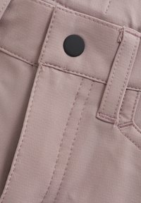 Ljust rosa tyg på nära håll som visar en knapp, sömnadsdetaljer och fickkonstruktion. Slät textur med subtil glans.