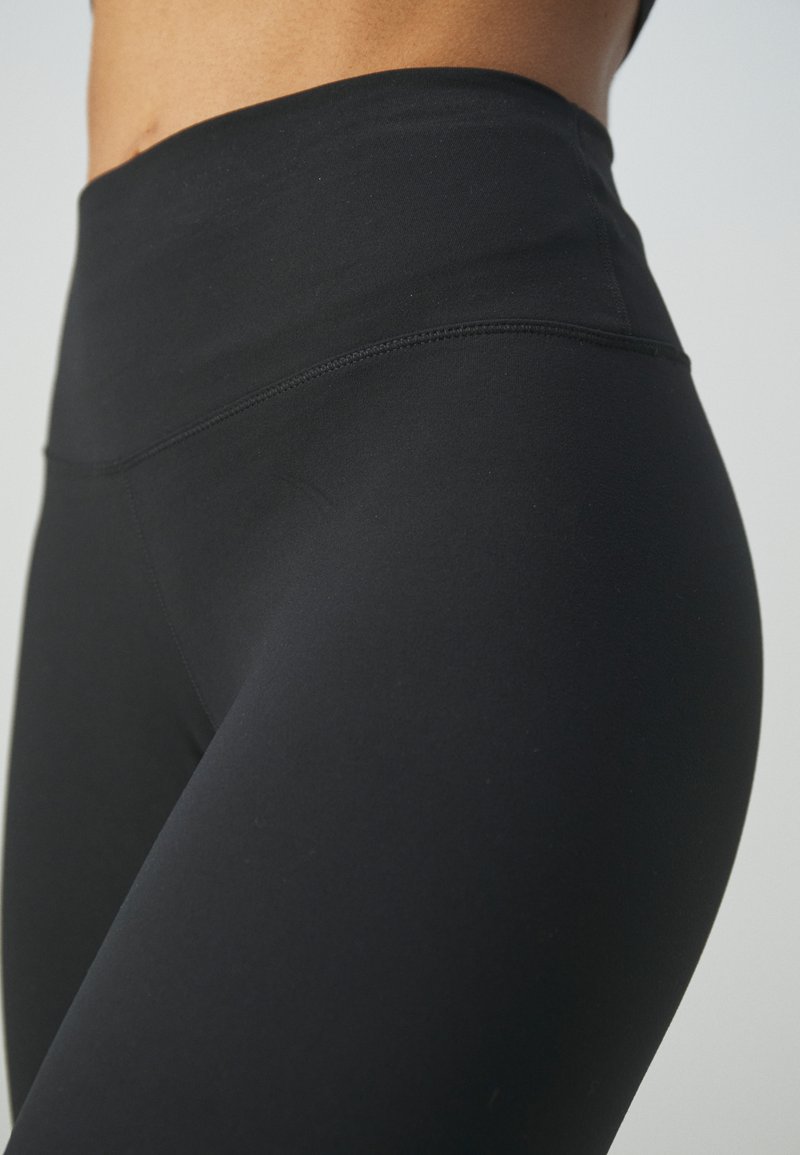 Leggings noirs taille haute en matière lisse et extensible avec un design sans coutures et des coutures discrètes, offrant une silhouette ajustée.