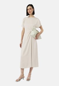 Jasno beżowa sukienka do kolan z krótkimi rękawami i skręconym detalem z przodu. Połączona z jasnym torebką i sandałami na obcasie.