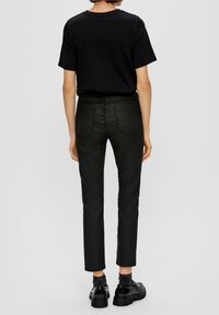 Svart bomullst-shirt i kombination med slim-fit svarta jeans, med bakfickor och ankellängd. Skorna är svarta med en blank ytfinish.