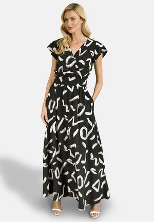 Black maxi dress with white abstract brushstroke patterns, short sleeves, V-neck, and an elastic waist. Model wears white heels.
