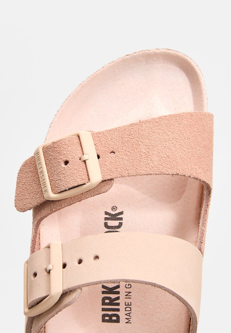 Nahaufnahme einer pinken Birkenstocksandale mit zwei verstellbaren Wildlederriemen und Schnallen auf einem weißen Hintergrund.