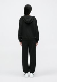 Czarny zestaw z bluzy z kapturem i spodni dresowych wykonany z miękkiej tkaniny, z kapturem ze ściągaczem, ściągaczami na mankietach i elastycznym pasem dla wygody.