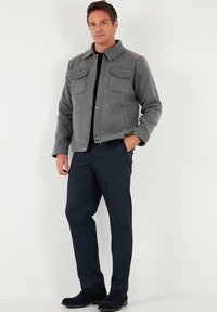 Jachetă gri din lână cu guler, două buzunare la piept și închidere cu nasturi, asortată cu pantaloni bleumarin și cizme închise la culoare.