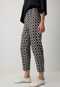 Black and cream patterned pants with a geometric design, high waist, tapered legs, and side pockets, paired with white lace-up shoes.