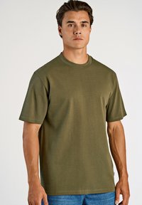 Olivgrön bomullströja med rund halsringning och korta ärmar, som har en avslappnad passform och minimala sömmar. I kombination med blå denimjeans.