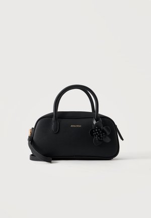 Sac à main en cuir noir avec double poignée et décoration fleurie sur le devant, équipé d'une fermeture éclair dorée et d'une bandoulière ajustable.