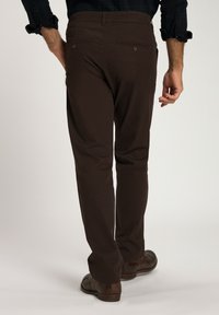 Bruna bomullsbukser med rak snitt, bakfickor med knappar och en slät yta. Bärs med mörka skor.