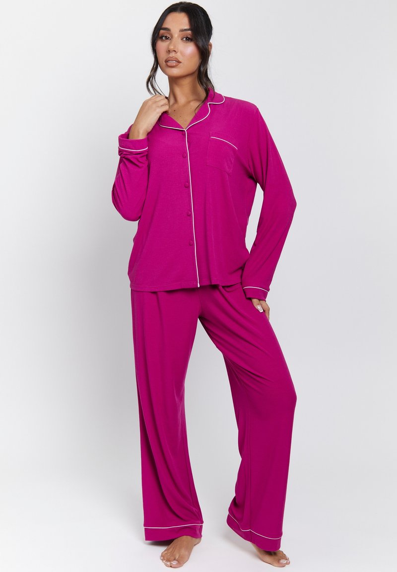 Conjunto de pijama magenta hecho de una tela suave. Parte superior de manga larga con botones y un bolsillo en el pecho, combinado con pantalones de pierna ancha con un ribete contrastante.