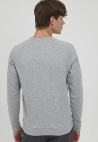 Grå sweatshirt med et struktureret, glat stof. Har raglanærmer og ribbet hals og kant. Enkel design uden synlige mønstre eller accenter.