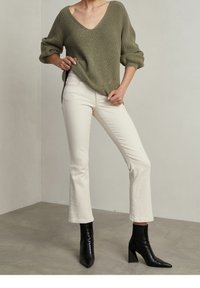 Oliivinvihreä neulepusero, jossa on V-kaulus, yhdistetty valkoisiin leveälahkeisiin farkkuihin ja mustiin korkokenkiin. Teksturoitu kangas ja ribbireunat.