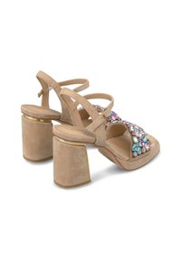 Beige suède hoge hakken sandalen met een chunky hak, voorzien van een sierlijke embellishment aan de voorkant. Inclusief verstelbare enkelband.