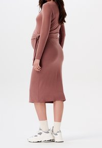 Těhotenské šaty v mauve s dlouhými rukávy a uzlovým detailem v pase. Kombinované s bílými teniskami a béžovými ponožkami. Hladká látka.