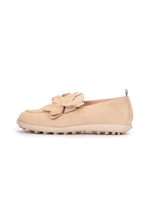Mocassin plat beige avec semelle en caoutchouc texturée et grande fleur superposée en décoration sur le dessus, vue de côté sur fond blanc.