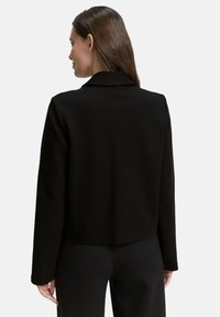 Black tailored jacket with a structured collar, smooth texture, and long sleeves, featuring a cropped design and minimalistic style.