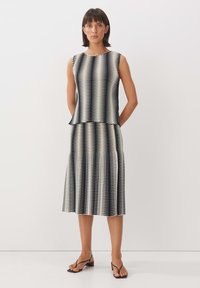 Top senza maniche a righe bianche e nere abbinato a una gonna coordinata, con un design svasato e tessuto texturizzato, completato da sandali con cinturini.