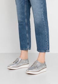 Chaussures montantes argentées métalliques avec une texture lisse, un bout rond et une semelle compensée, associées à un jean bleu en denim longueur cheville.