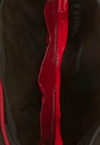 Interior de bolsa negra con un forro rojo. Presenta una textura suave, cierre con cremallera y sin compartimentos ni adornos visibles.